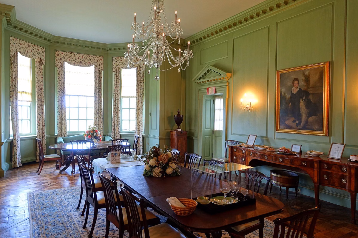 The Dining Room in the Great House, with a long table, chandelier and portrait