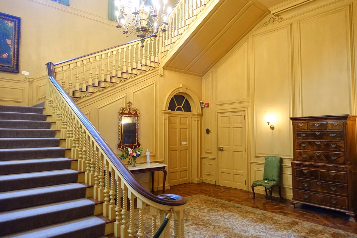 The Stair Hall of the Great House, with the grand staircase and a chest of drawers