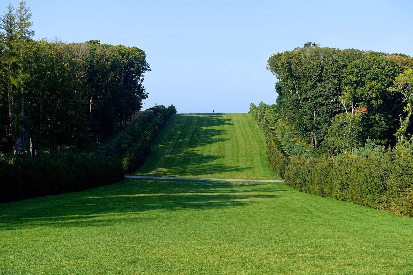The Grand Allée at Castle Hill, a long lawn between hedges and trees leading toward the sea